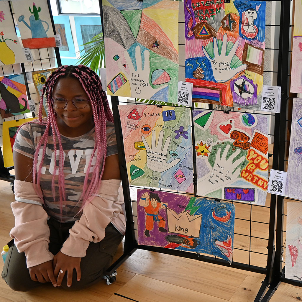 Student posing in front of her work displayed at the Leimert Park Village creative space.